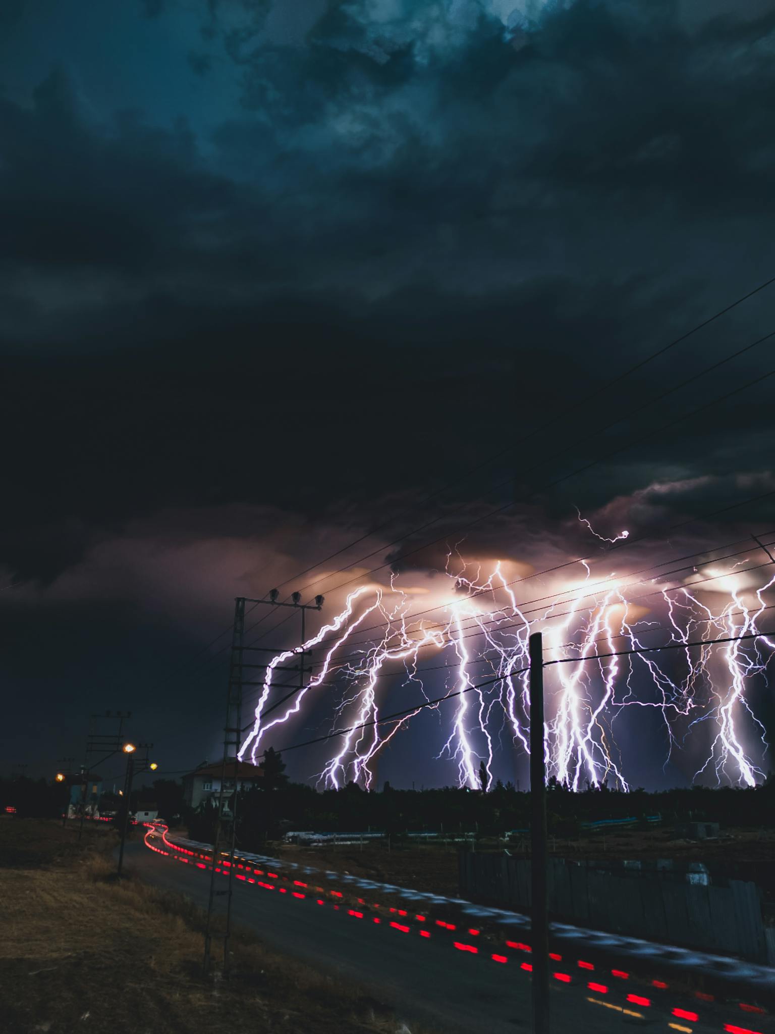 A dramatic thunderstorm with bright lightning bolts striking above a city skyline at night.