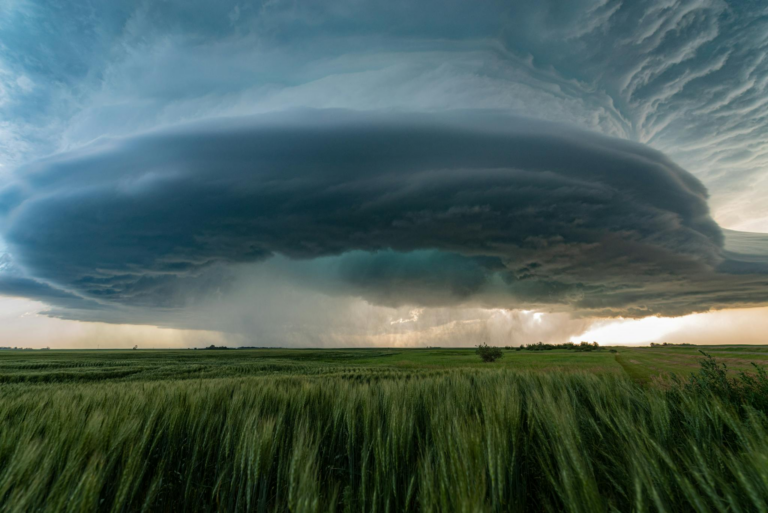 A powerful supercell storm looms over lush green fields in Saskatchewan, Canada.